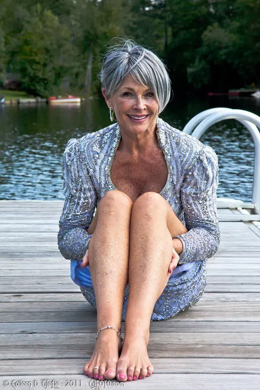 Older woman with gray hair wearing gray dress sitting on a dock