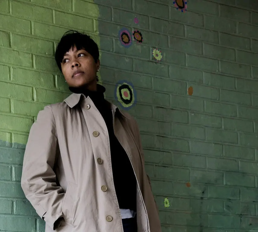 African American woman in trenchcoat standing against green wall
